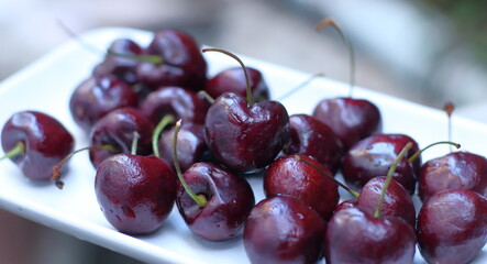 Red cherries with stems in a white plate on a wooden background