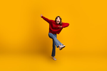 Fototapeta premium Energetic young female on a bright yellow background expressing joy through a playful pose in modern casual fashion