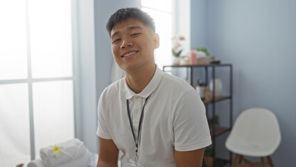 Fototapeta premium Young chinese man smiling in a spa wellness center, showcasing a serene indoor setting with soft lighting and a minimalist interior.