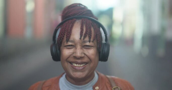 Happy senior african woman listening music with wireless headphone in the city - Travel, urban and elderly lifestyle concept 