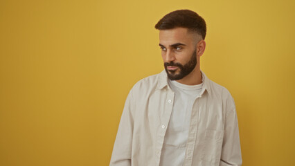 Young hispanic man with a beard standing in front of an isolated yellow background