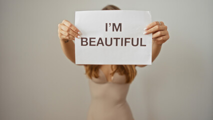 Young woman holding a sign with 'i'm beautiful' text against white background capturing the essence...
