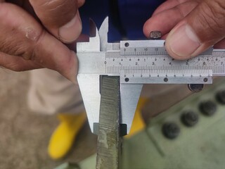 Close-up of hands using a caliper to measure a metal beam for precise engineering work