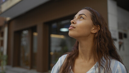 Woman looking thoughtful standing on an urban street during daytime, featuring a young, beautiful,...