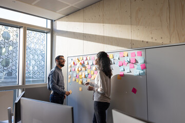 Coworkers discussing business strategy using adhesive notes to brainstorm in an office