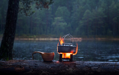 Boiling water in a kettle on a portable solid fuel stove near a lake in the forests a rainy day in the autumn