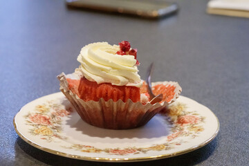 
a red velvet cupcake with a white cream hat and a red berry on top, placed on a floral patterned porcelain plate.
