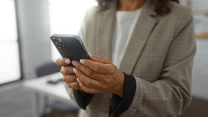 Woman using smartphone in modern office, wearing business attire, focused on communication and technology, adult female professional setting, indoors, neatly dressed, working.
