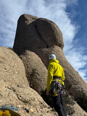 A man in a yellow jacket stands on a rocky mountain, looking up at a large rock