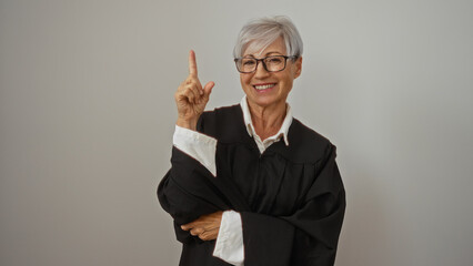 Elderly woman with grey hair and glasses wearing a judge robe isolated on white background pointing upwards while smiling joyfully