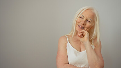 Woman with albinism stands smiling and thoughtful against a white wall background, showcasing her...