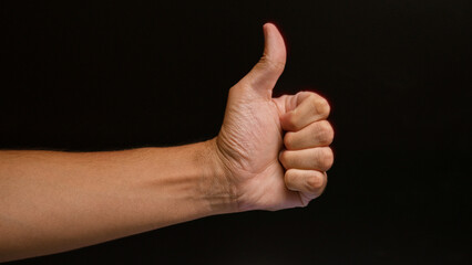 Man showing a thumbs-up sign with a close-up of his hand against a dark background, illustrating approval or positivity