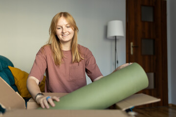 Young cheerful woman in glasses getting parcel at home. Pretty girl sitting on sofa at home and opening carton box. Express delivery service and satisfied consumer. Online shopping banner