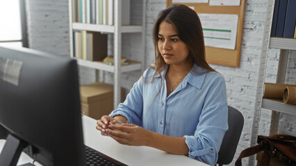 Young woman working in an office, seated at a desk with a monitor in front of her, showing a...
