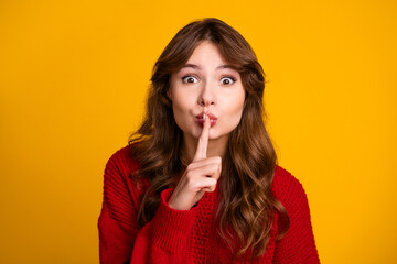 Naklejka premium Young woman making hush gesture with finger on lips, posing against bright yellow background