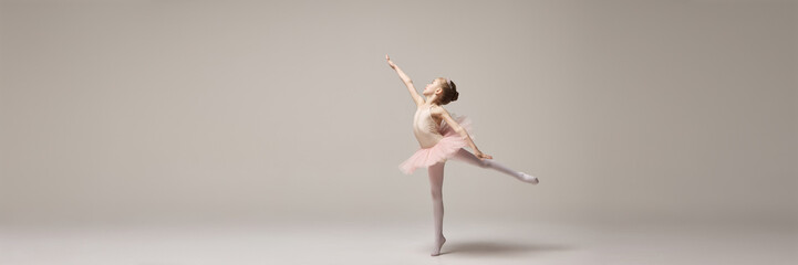 Banner. Little ballerina posing in arabesque position with arms forming graceful move against white...