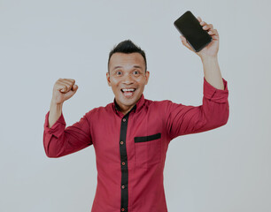 Asian man cheering happy while holding his mobile phone, isolated over white background.