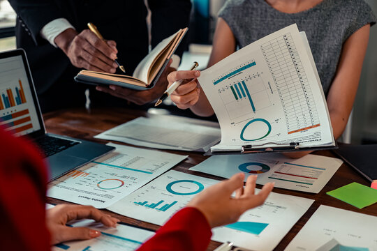 A group of financial analysts work together to discuss company financial statistics reports. Brainstorming with documents, graphs on the table, close-up image