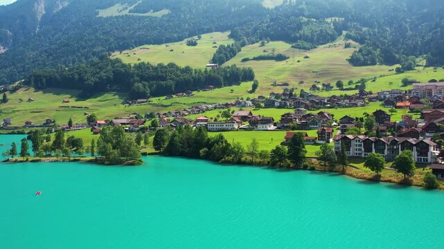 Drone footage of turquoise clear lake Lungern or Lungerersee in Switzerland in summer sunny day with village and green meadow