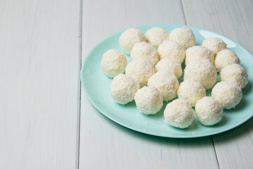 Blue plate with delicious homemade candies with coconut flakes and almonds stands on a light wooden table, background with copy space