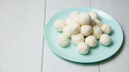 Blue plate with delicious homemade candies with coconut flakes and almonds stands on a light wooden table, background with copy space