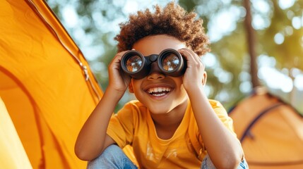 A smiling young boy sits inside a colorful tent, looking through his binoculars with glee, capturing the essence of childhood curiosity and camp adventure under a bright sky.