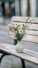 A single ceramic vase holding fresh flowers placed on a light-colored city bench. picture