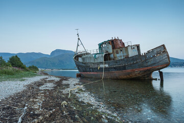 shipwrecked boat on shoreline with mountains in background
