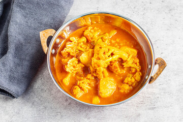 a bowl of vibrant yellow curry featuring cauliflower and potatoes, served in a traditional Indian-style copper dish.