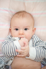 child beautiful happy boy with black eyes holds hands in mouth, close-up
