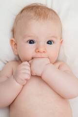 small beautiful baby with blue eyes holding his hands in his mouth