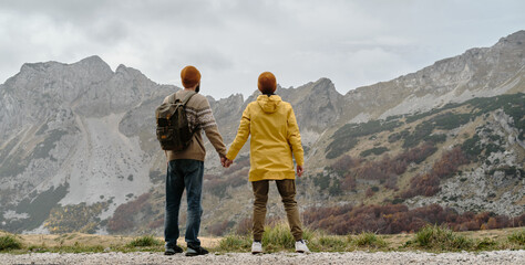 Naklejka premium Breathtaking mountain landscape with happy young couple holding their hands. Rear view. Travel around the world concept. Montenegro country, Durmitor National Park. Saddle Pass in autumn season