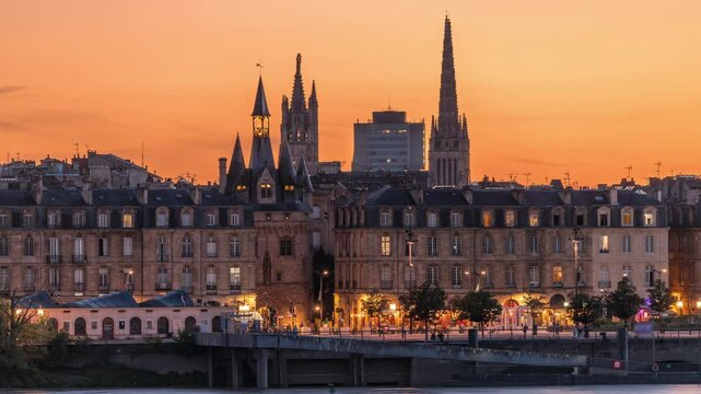 Panoramic view of Bordeaux city skyline day to night transition timelapse featuring Saint Michel Cathedral spires and Garonne River after sunset. Historic architecture, illuminated landmarks in France