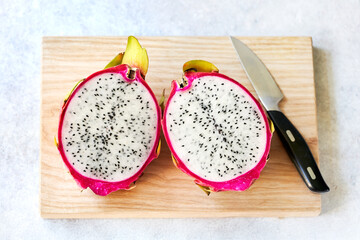 Halved dragon fruit on wooden board with knife. Top view. Flat lay.