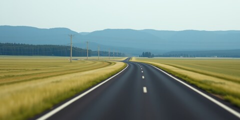 Fototapeta premium Asphalt road stretching towards a hazy mountain range, bordered by a field of golden grain