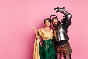 Young couple dressed in medieval knight and princess costumes on a pink background, themed party concept