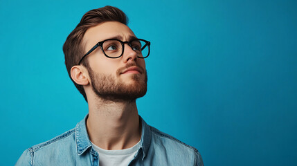 Obraz premium A professional yet casual portrait of a man with a beard and glasses, dressed in a blue denim jacket, isolated on a blue background