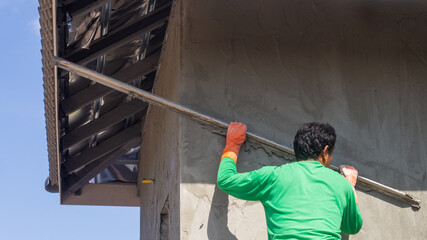 Plastering the cement wall of an outdoor house building with workers working on a construction site