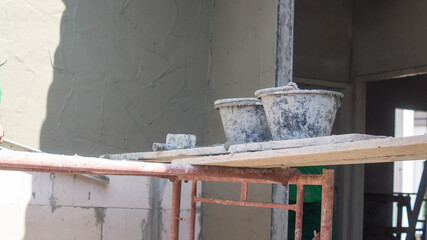 Plastic bucket for putting cement in wall plastering work. It rests on a plank placed between two sides of scaffolding in the construction site.