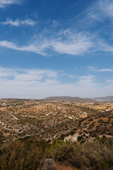 Landscape featuring rolling hills covered in dry vegetation, winding paths and blue sky