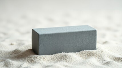 A solitary, rectangular, gray block rests gently upon a bed of fine, white sand, creating a minimalist scene.