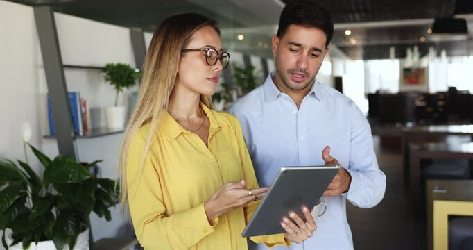 Workmates using tablet standing in coworking space during break, review documents or presentation, collaborate on project, look up information or trends relevant to their work, go over analytical data