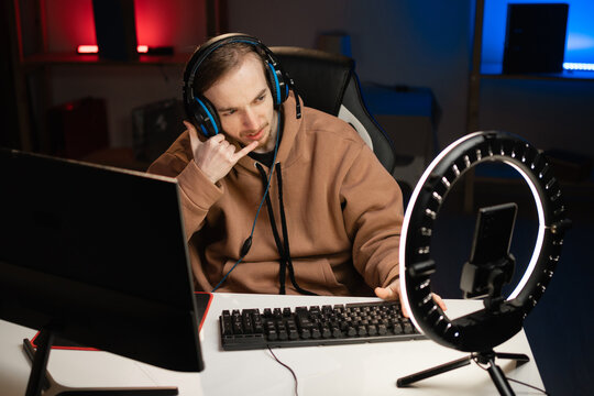 blogger gamer broadcasts live streaming to review video game on social media, doing phone gesture like says call me, reviews for video blog. Influencer uses smartphone and ring lamp.