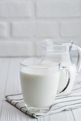 milk in glass cup and in jug on table with white brick wall on the background