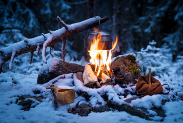 Coffee kettle hanging on a branch over a camp fire in a snow-clad forest