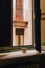 A serene morning scene showing a cup of coffee on a windowsill, looking out to an urban balcony with soft architecture. Perfect for themes of relaxation and peaceful urban life.