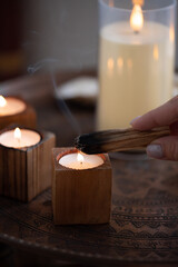 A stick of palo santo incense in a woman's hand smolders against the background of candles