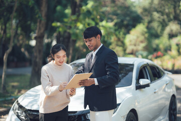 Car Dealership Consultation: A friendly and professional sales representative explains the details of a car purchase agreement to a smiling female customer, standing in front of a sleek car outdoors.