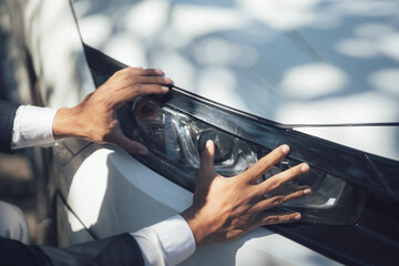 Close-up Inspection: A man's hands gently caress the sleek headlight of a modern car, conveying a sense of appreciation for automotive design and luxury.