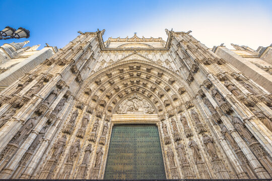 Seville Cathedral, The Cathedral of Saint Mary of the See in Seville town, Andalusia, Spain, Europe. Ornate cathedral entrance, detailed stone carvings, imposing architecture under a clear blue sky. - Powered by Adobe